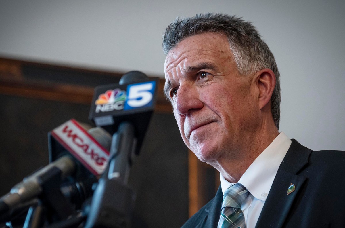 A man in a suit speaks at a podium with microphones from NBC5 and WGAN.